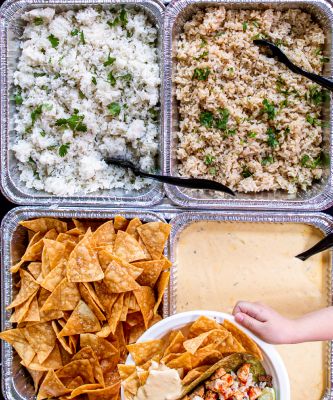 Catering trays with white and brown rice, chips, and queso.