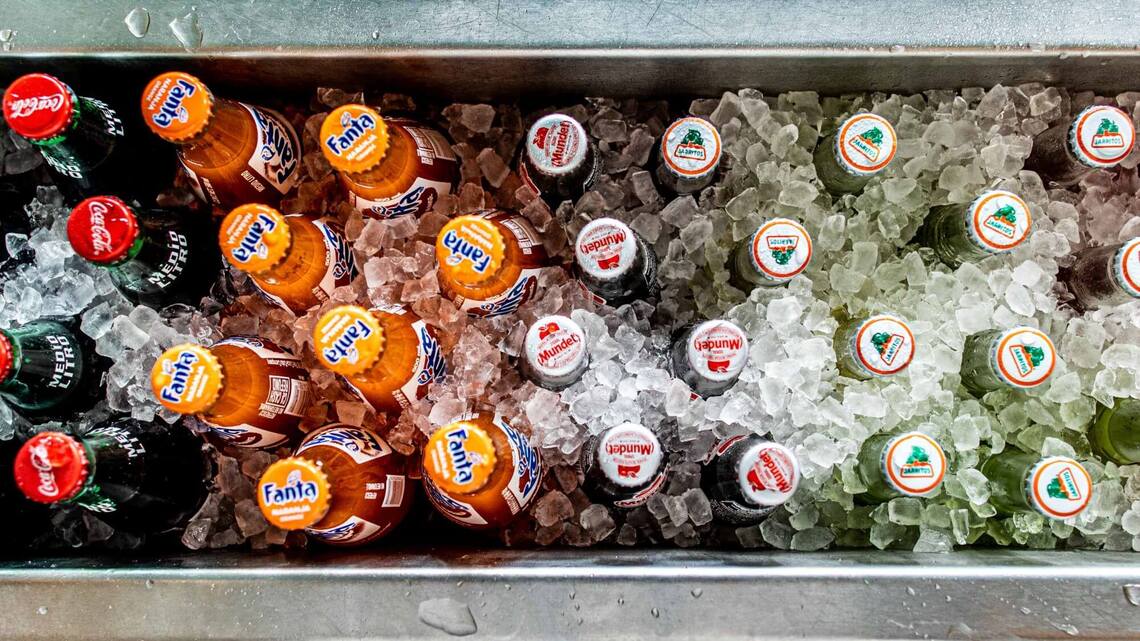 Glass bottles of Fanta and Coca Cola viewed from the top with ice around the bottles.