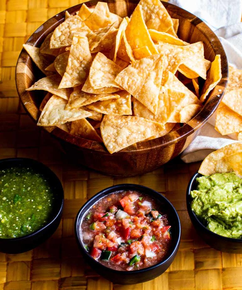 A bowl of chips next to smaller bowls of salsa.