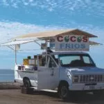 White truck with a shelter over it reading "cocos frios".