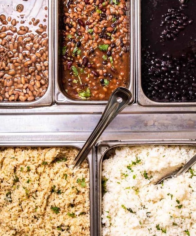 Build Your Own 9 Catering trays of rice and beans with spoons sticking out of them.